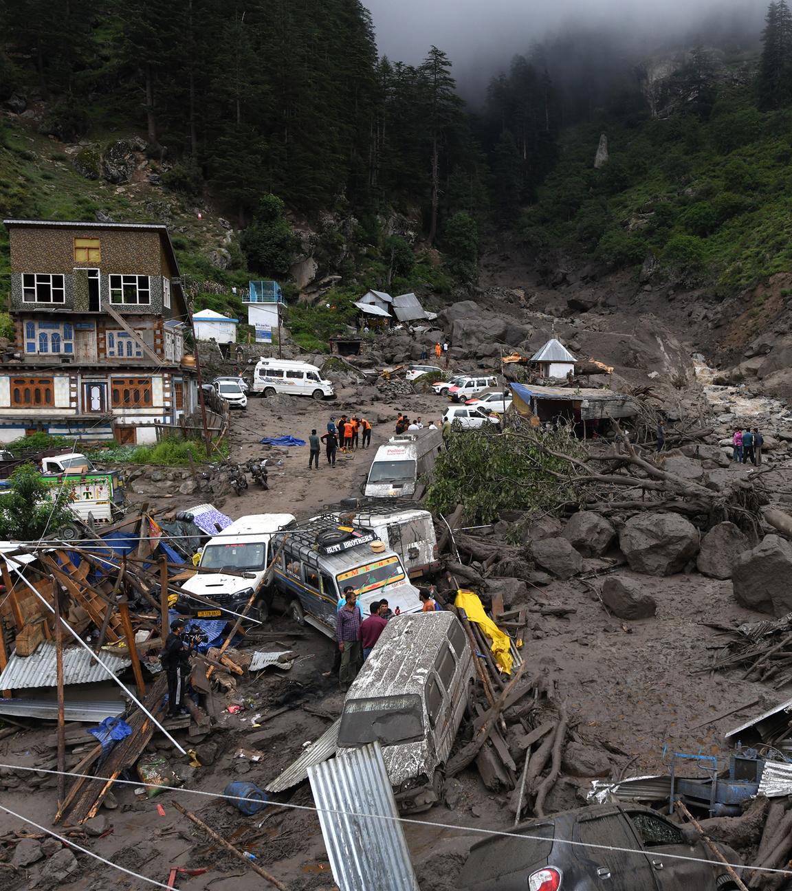 15.08.2025, Indien, Kishtwar: Rettungskräfte suchen zwischen Felsen und beschädigten Fahrzeugen nach Überlebenden und Opfern.