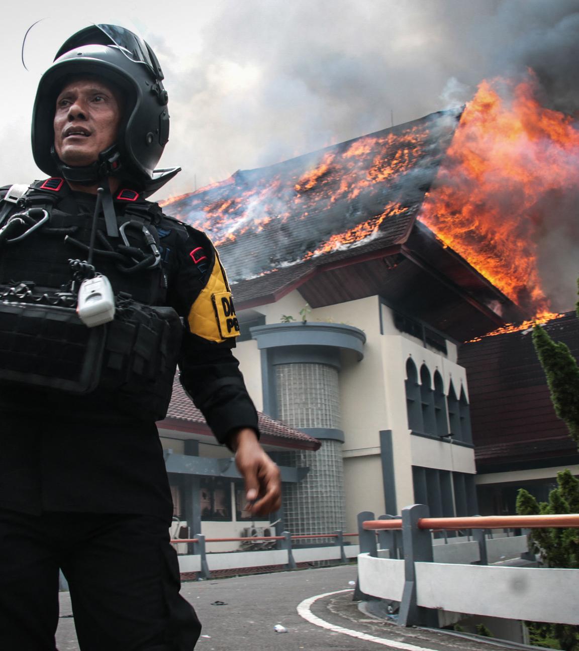 Ein Polizist steht mit einem Megafon da, während das Gebäude des Provinzrats von West-Nusa Tenggara brennt, nachdem es am 30.08.2025 von Demonstranten in Mataram auf der Insel Lombok, West-Nusa Tenggara, in Brand gesetzt wurde.