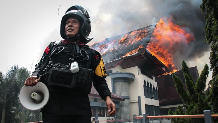 Ein Polizist steht mit einem Megafon da, während das Gebäude des Provinzrats von West-Nusa Tenggara brennt, nachdem es am 30.08.2025 von Demonstranten in Mataram auf der Insel Lombok, West-Nusa Tenggara, in Brand gesetzt wurde.