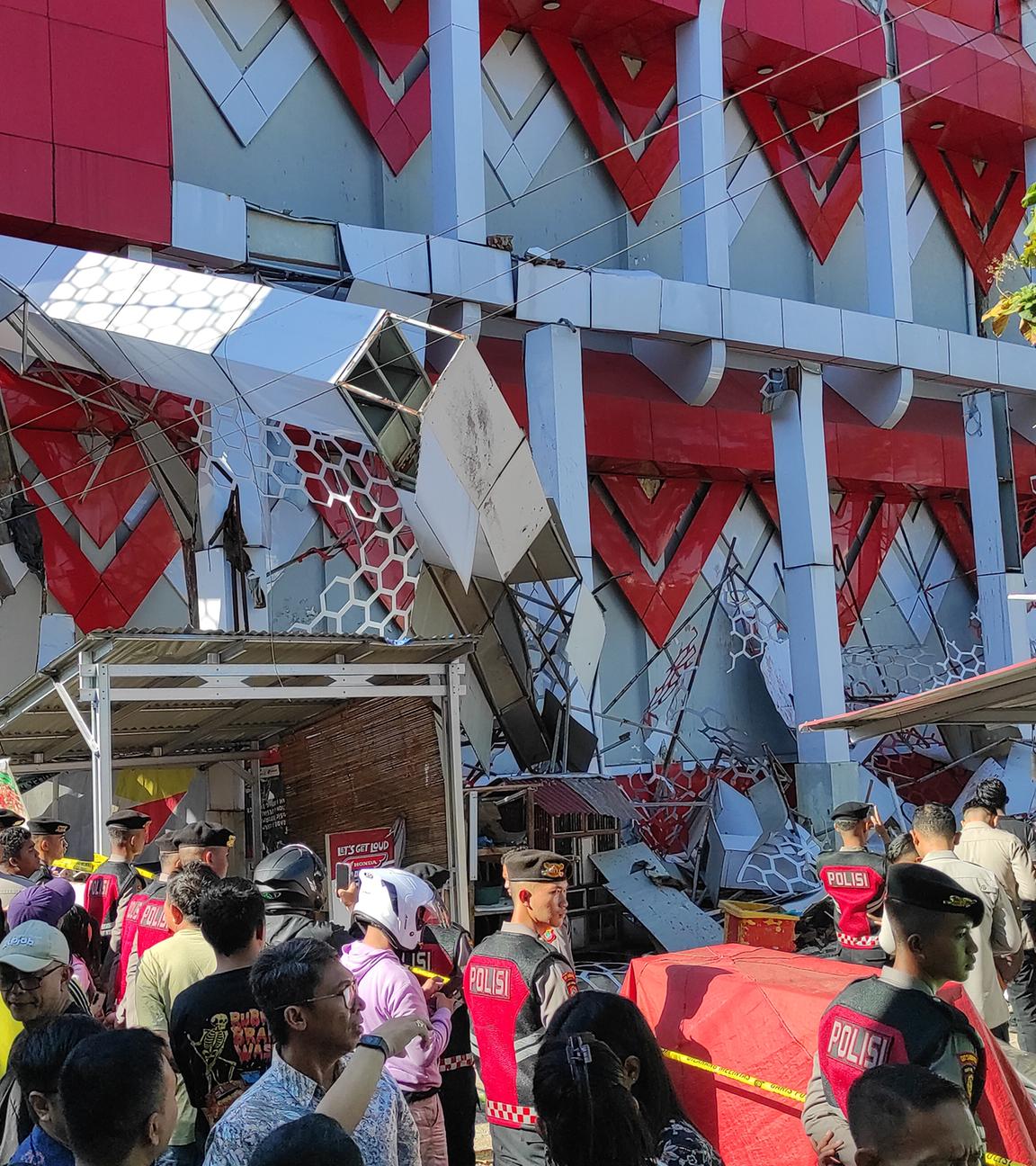 Schaulustige versammeln sich, während Polizeibeamte ein beschädigtes Gebäude nach einem Erdbeben in Manado, Nordsulawesi, Indonesien, inspizieren.