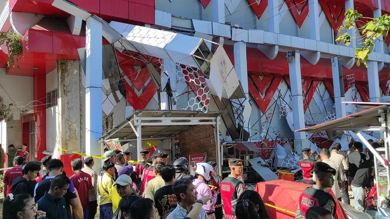 Schaulustige versammeln sich, während Polizeibeamte ein beschädigtes Gebäude nach einem Erdbeben in Manado, Nordsulawesi, Indonesien, inspizieren.