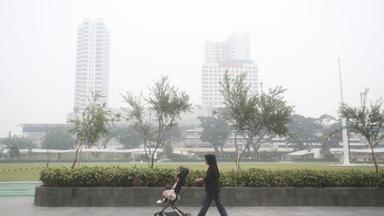 Eine Frau schiebt einen Kinderwagen in einem Park, während Rauch von Waldbränden die Stadt Medan in Nordsumatra einhüllt.