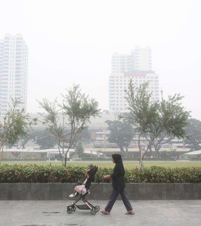 Eine Frau schiebt einen Kinderwagen in einem Park, während Rauch von Waldbränden die Stadt Medan in Nordsumatra einhüllt.