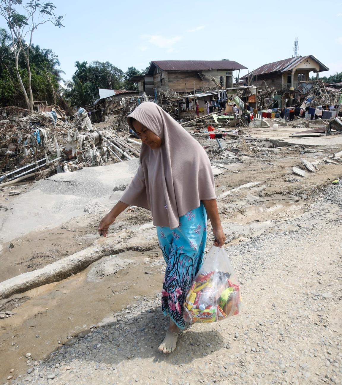 Eine Überlebende trägt Hilfsgüter in einem Gebiet, das von Sturzfluten in Aceh Tamiang auf der Insel Sumatra, Indonesien, am 05.12.2025, verwüstet wurde. 