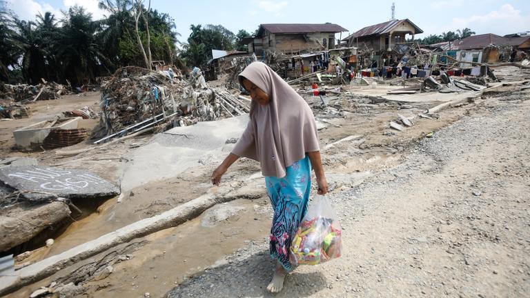 Eine Überlebende trägt Hilfsgüter in einem Gebiet, das von Sturzfluten in Aceh Tamiang auf der Insel Sumatra, Indonesien, am 05.12.2025, verwüstet wurde. 