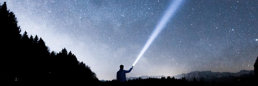 Ein Mensch leuchtet mit einer Taschenlampe in den Sternenhimmel.