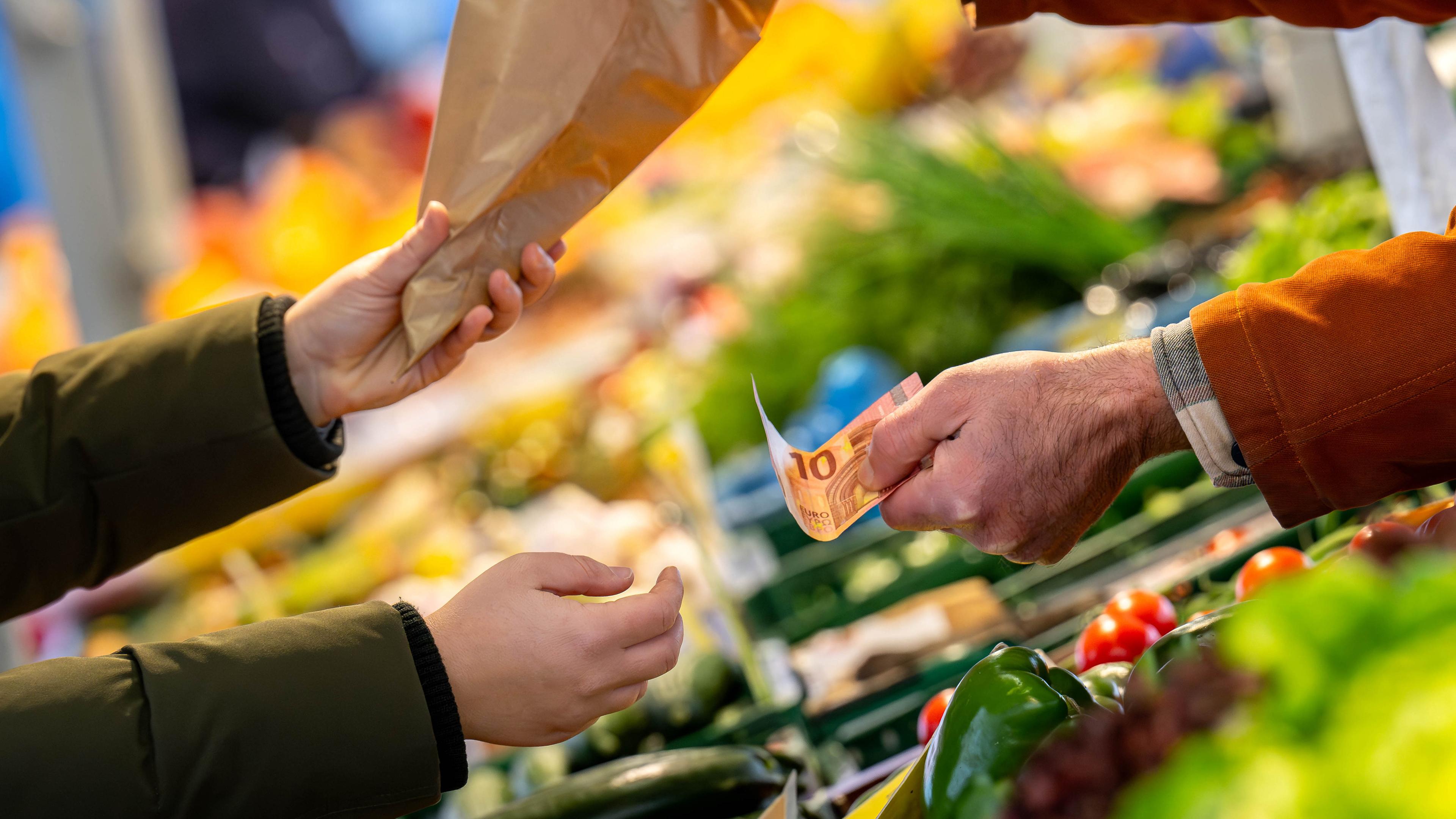 An einem Marktstand wird mit Bargeld eingekauft.
