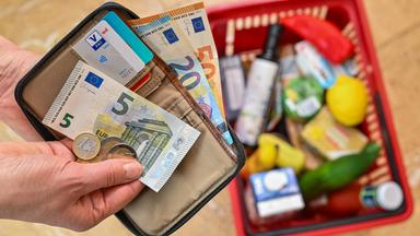 Brandenburg, Sieversdorf: Eine Frau hält auf ihrer Hand Geld vor einem vollen Einkaufskorb mit Lebensmitteln. 