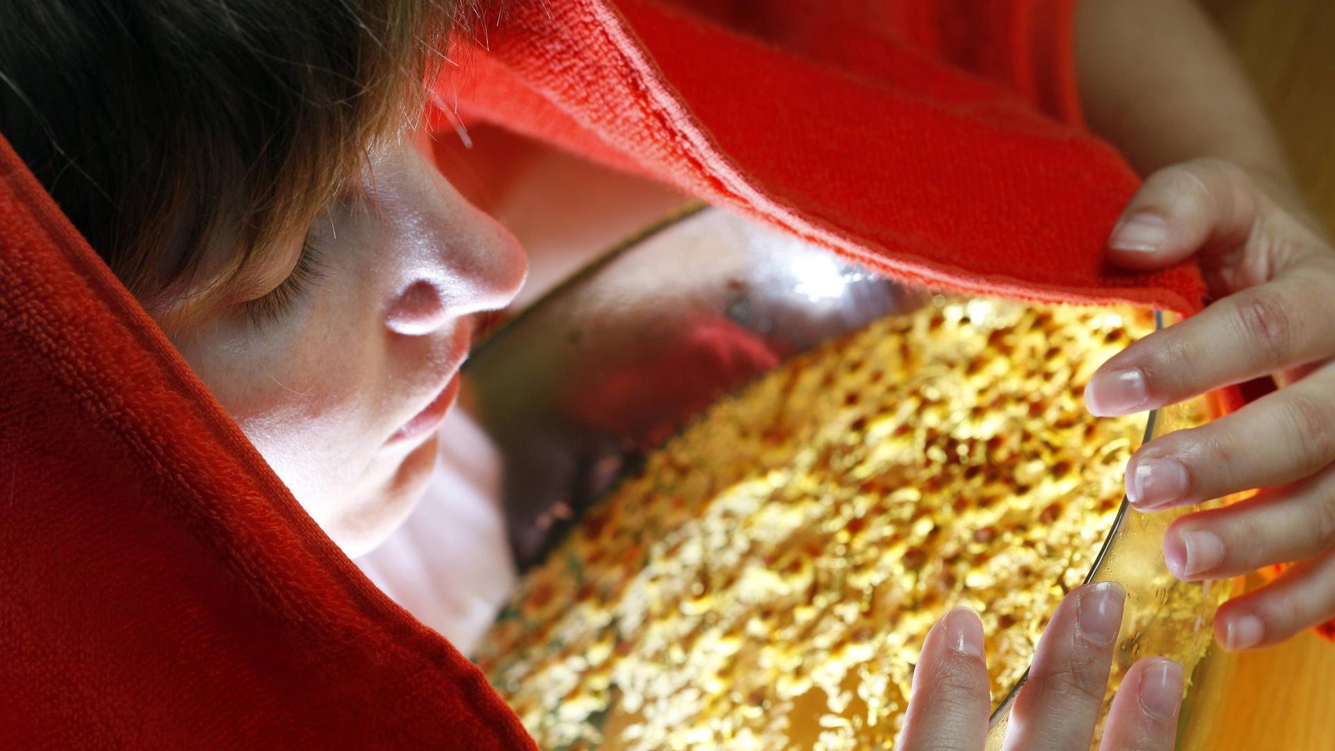 Eine junge Frau inhaliert die Dämpfe eines Kräuteraufgusses aus getrockneten Kamilleblüten .