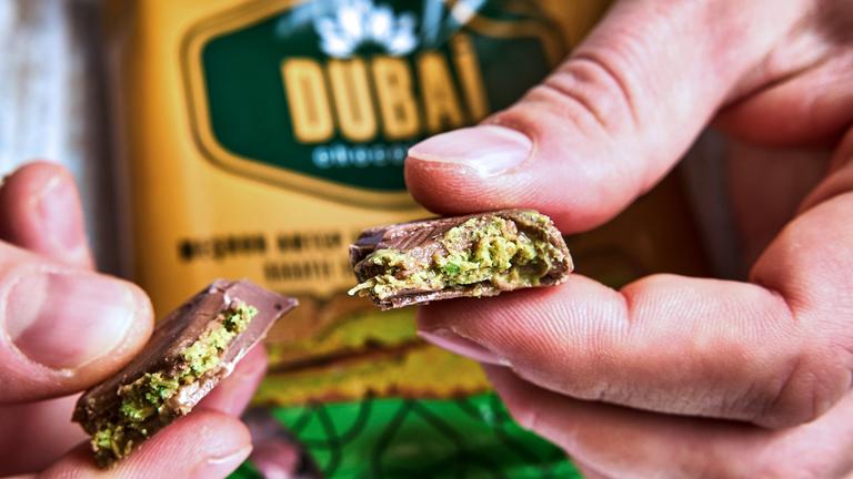 Ein Mann hält ein Stück der exklusiven Dubai-Schokolade vor die Verpackung