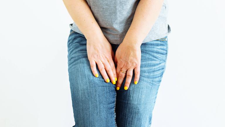 Eine Frau fasst sich so zwischen die Beine, als müsste sie dringend auf Toilette.