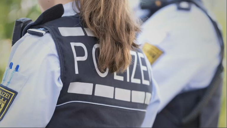 Zu sehen ist eine weibliche gelesene Person in Polizeiuniform mit dem Rücken zur Kamera.