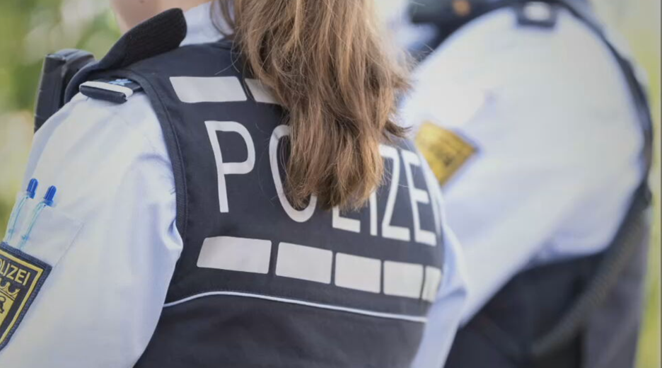 Zu sehen ist eine weibliche gelesene Person in Polizeiuniform mit dem Rücken zur Kamera.