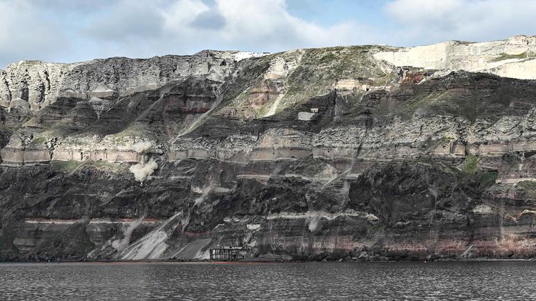 Felsstürze durch Erdrutsche, die durch Erdbeben verursacht wurden, wirbeln am 03.02.2025 Staubwolken entlang der Felswand auf der griechischen Insel Santorini auf