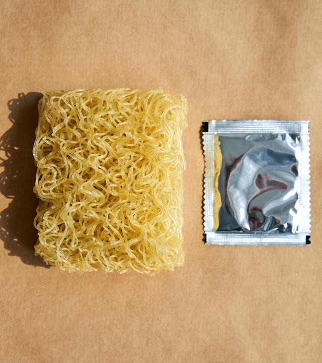 Trockene Instantnudeln mit Gewürzpackung auf braunem Hintergrund.