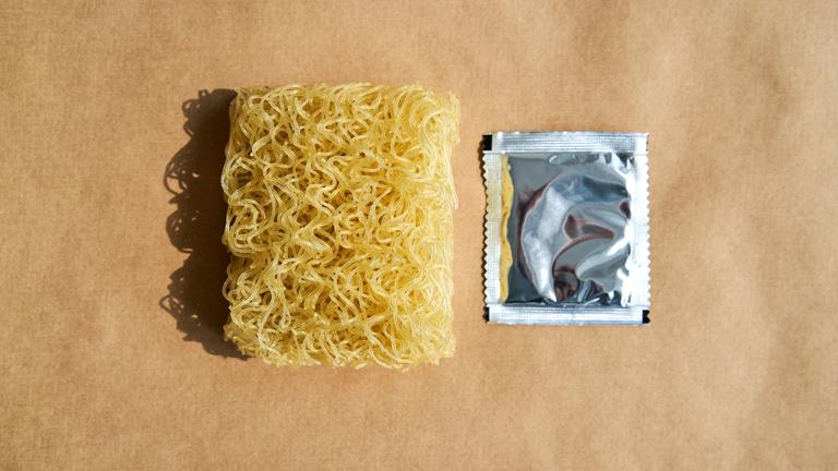 Trockene Instantnudeln mit Gewürzpackung auf braunem Hintergrund.