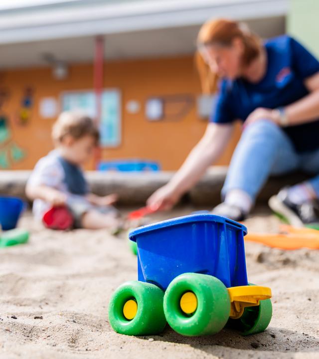 Eine Erzieherin spielt mit einem Kind im Sandkasten einer Kita.