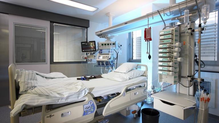 Ein leeres Bett auf der Intensivstation umgeben von medizinischen Geräten für die Versorgung, Beatmung und Überwachung des Patienten.