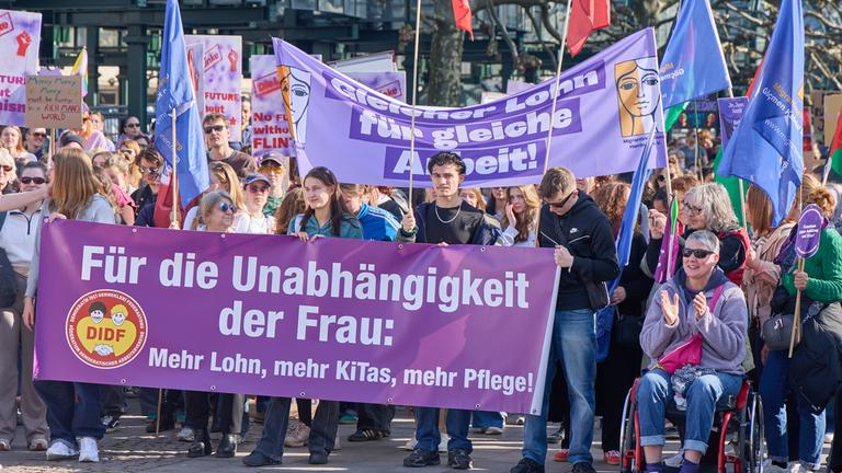 eilnehmerinnen und Teilnehmer einer Demonstration zum Frauentag halten auf dem Rathausmarkt in Hmaburg ein Trandparent mit der Aufschrift "Für die Unabhängigkeit der Frau: Mehr Lohn, mehr Kitas, mehr Pflege!"