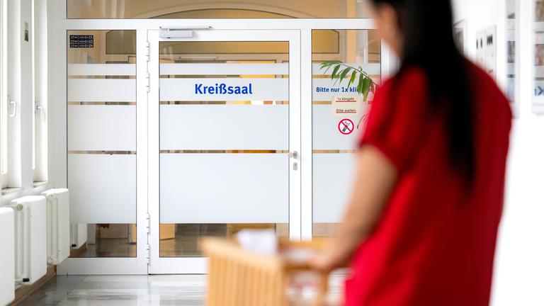 Eine Hebamme schiebt ein Bett mit einem Säugling zum Kreißsaal.