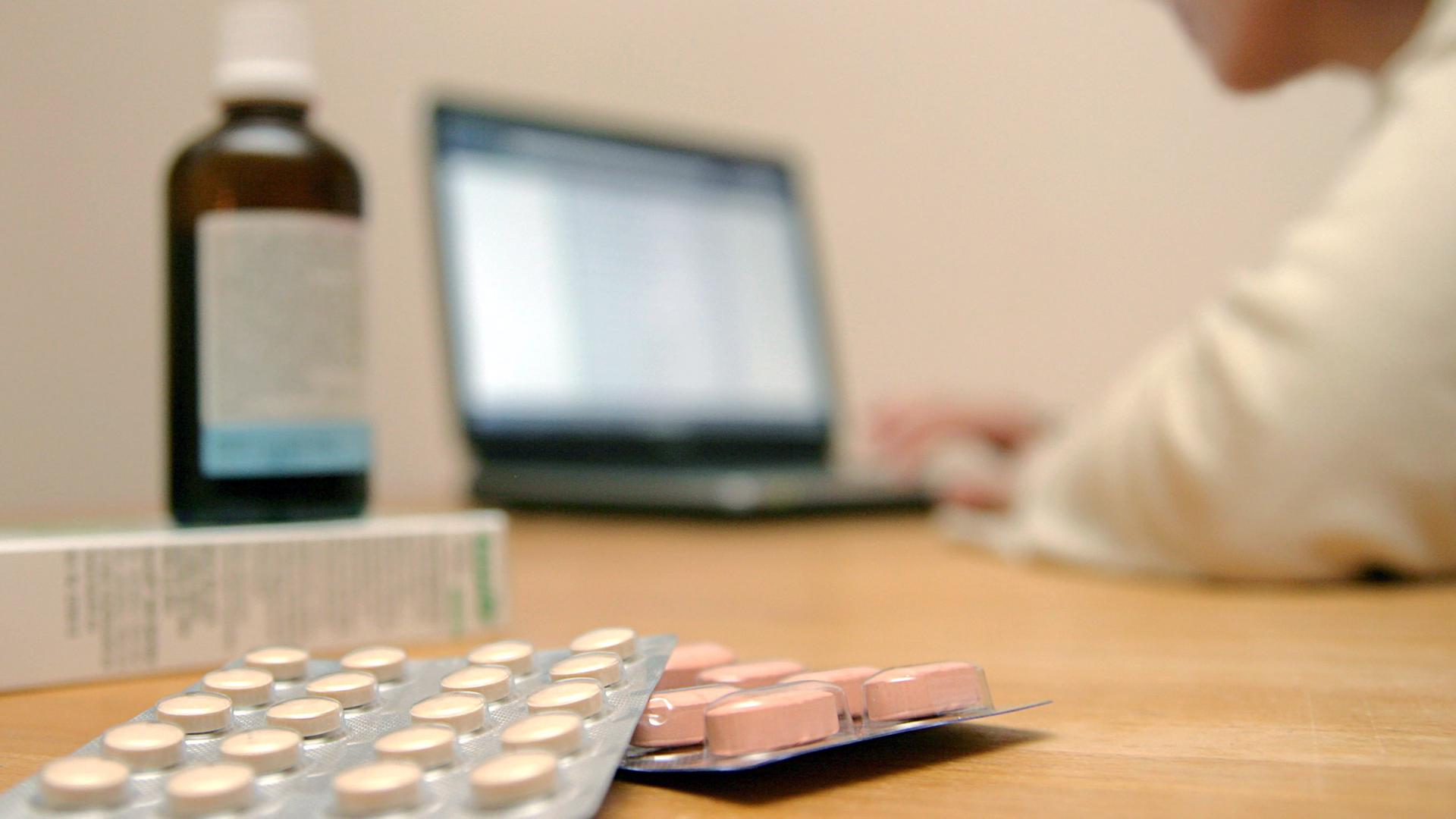 Eine Frau bestellt in Internet ihre Arzneien, von denen ein paar Proben auf dem Tisch liegen, Symbolbild