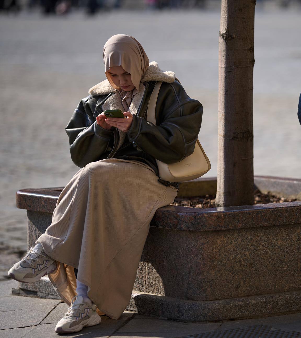 Eine Frau mit Kopftuch und eine weitere Frau sitzen am Roten Platz in Moskau und halten jeweils ein Smartphone in der Hand.