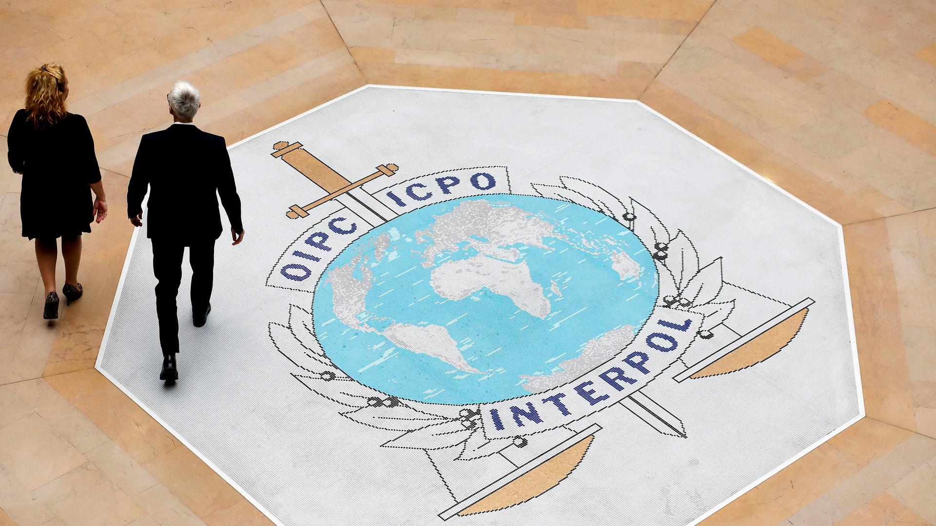 Zwei Männer gehen über ein Logo von Interpol, das in den Boden eingelassen ist. 