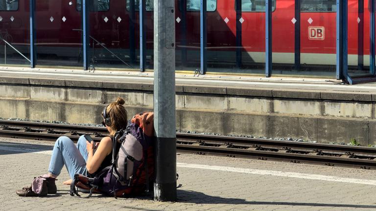 Eine junge Rucksacktouristin sitz am Bahnsteig