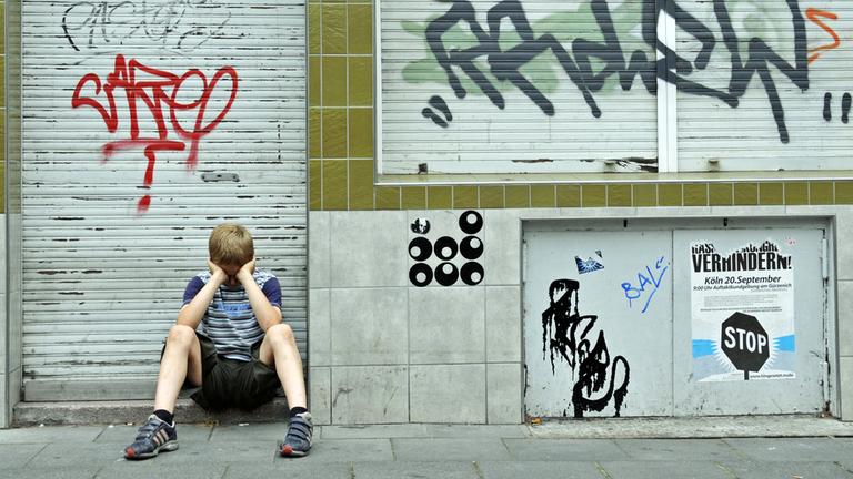 Einsamer Junge vor verschmierter und geschlossener Ladenfassade.