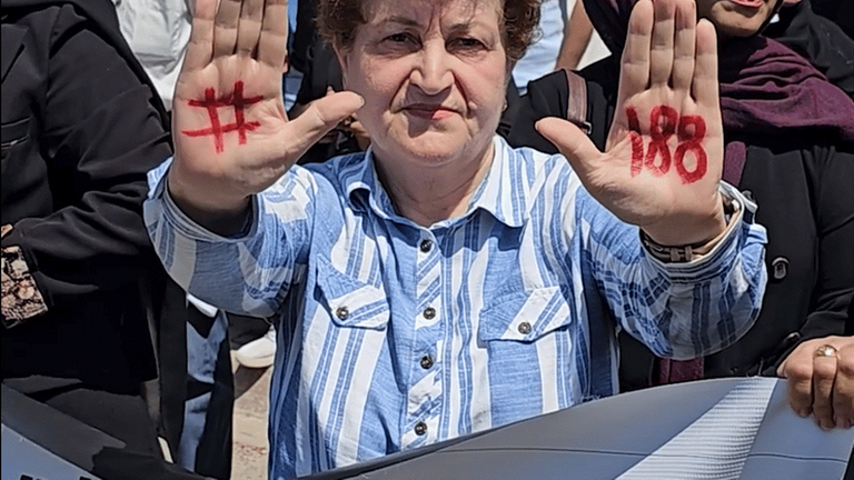 Eine ältere Frau hält ihre mit einer Raute und mit einer "188" beschrifteten Handflächen nach oben.