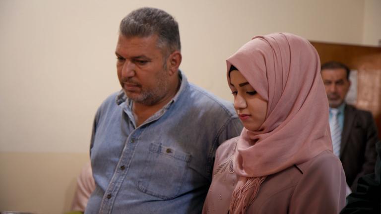 "Iraks geheimer Frauenhandel - Versklavt, verkauft, vergessen": Ein Mann läuft neben einer jungen Frau, die einen rosafarbenen Schleier trägt und ihren Kopf gesenkt hält.