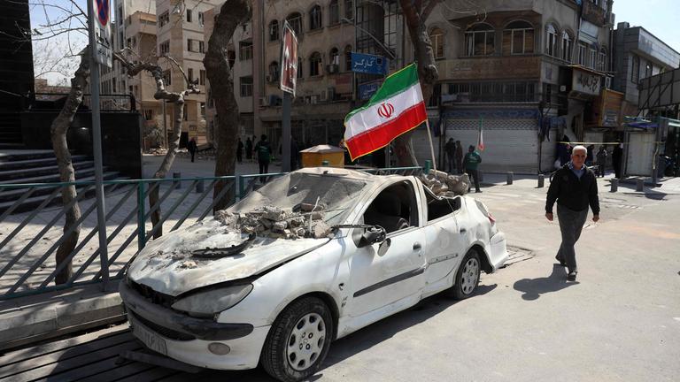 Mann läuft an einem von US-Angriff zerstörten Auto in Teheran vorbei.