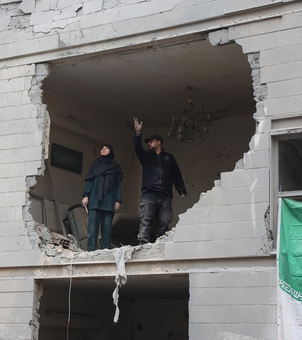 Zwei Iraner stehen in einem zerstörten Gebäude im Süden von Teheran vor einem großen Loch in der Wand.