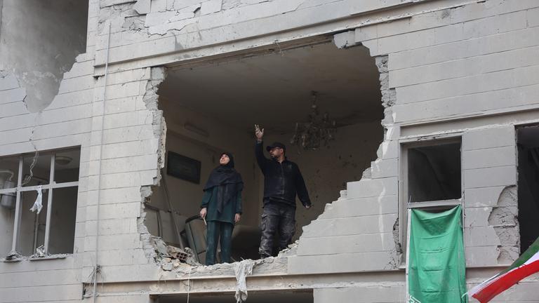 Zwei Iraner stehen in einem zerstörten Gebäude im Süden von Teheran vor einem großen Loch in der Wand.