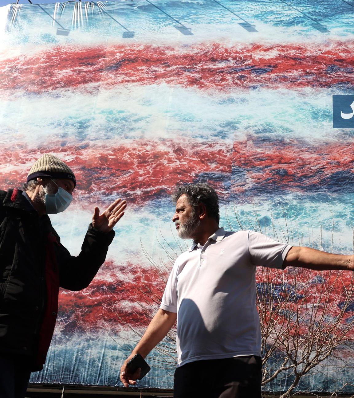 Iraner unterhalten sich vor einer Anti-USA-Werbetafel in Teheran am 25. Februar 2026, kurz vor der Wiederaufnahme der dritten Runde der Atomgespräche in Genf.