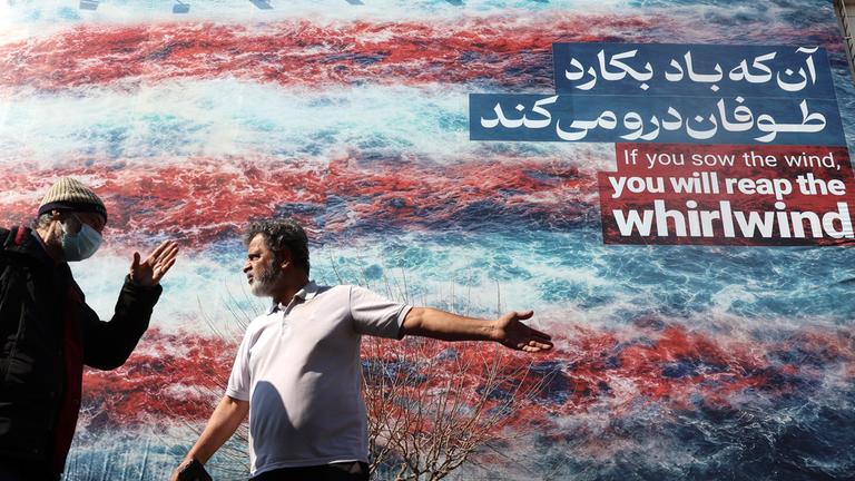 Iraner unterhalten sich vor einer Anti-USA-Werbetafel in Teheran am 25. Februar 2026, kurz vor der Wiederaufnahme der dritten Runde der Atomgespräche in Genf.