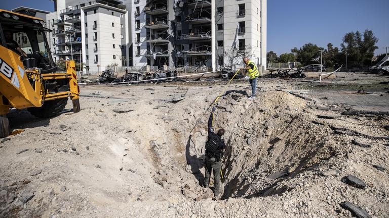 Israelische Polizeibeamte und Bombenentschärfungsexperten sind bei der Arbeit an der Einschlagstelle zu sehen, nachdem eine angeblich aus dem Iran abgefeuerte Rakete am 20. Juni 2025 in der südisraelischen Stadt Beersheba eingeschlagen ist.
