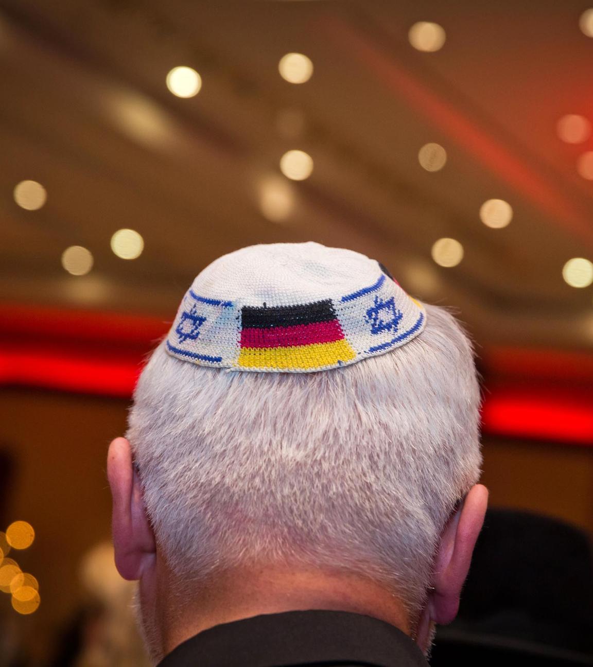 Kopf eines weißhaarigen Mannes von hinten mit Kippa mit deutscher und israelischer Flagge
