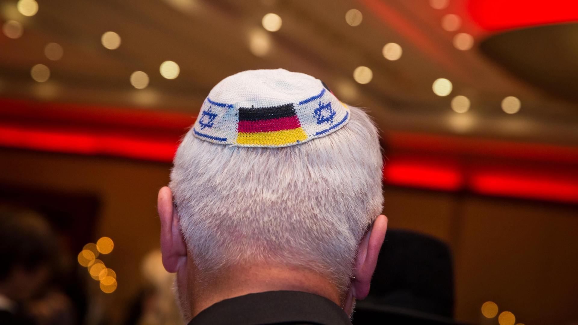 Kopf eines weißhaarigen Mannes von hinten mit Kippa mit deutscher und israelischer Flagge