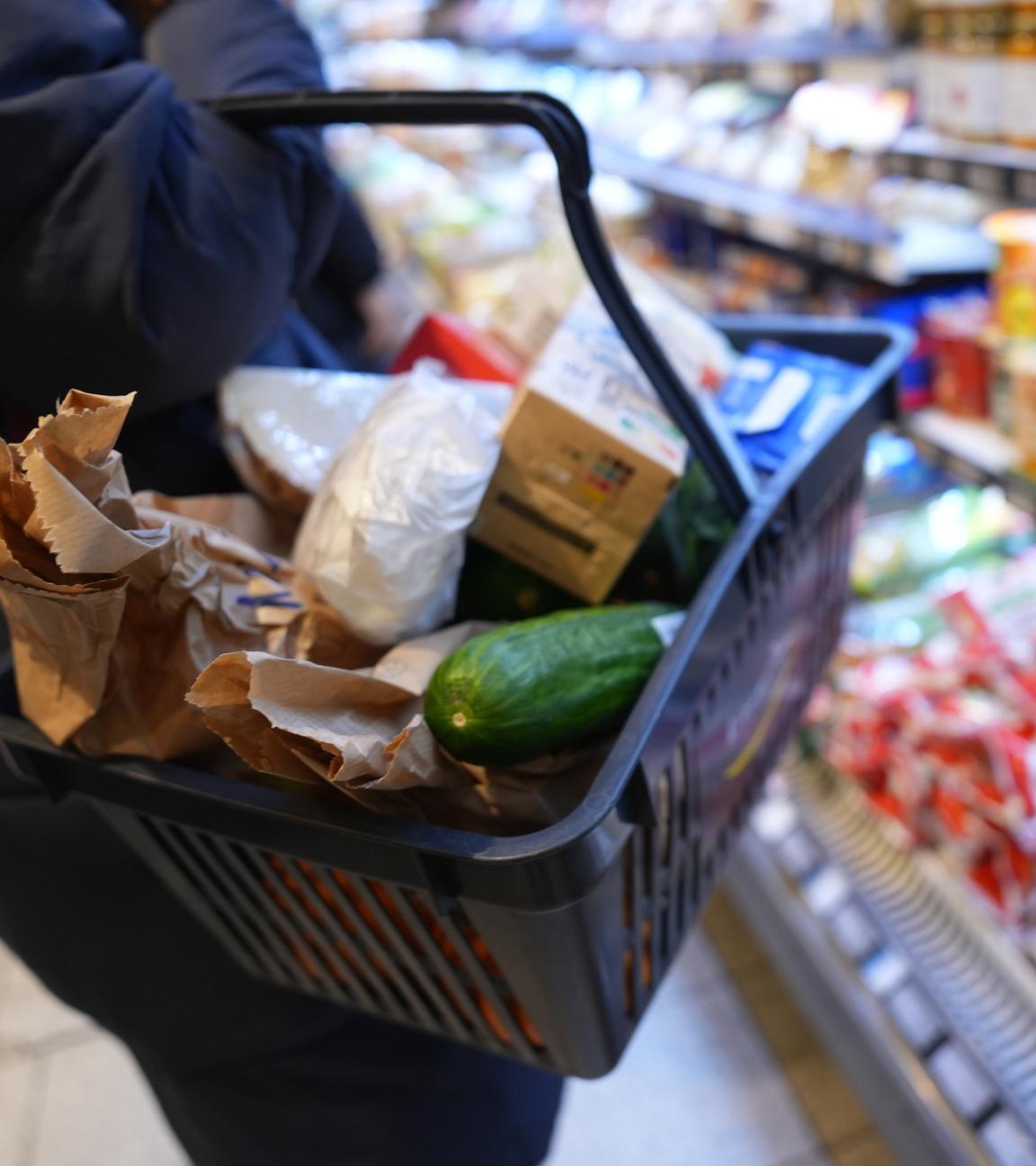 Eine Kundin geht mit einem Einkaufskorb und ihrem Einkauf an den Regalen in einem Supermarkt vorbei.