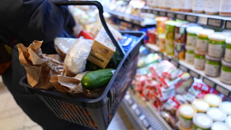 Eine Kundin geht mit einem Einkaufskorb und ihrem Einkauf an den Regalen in einem Supermarkt vorbei.
