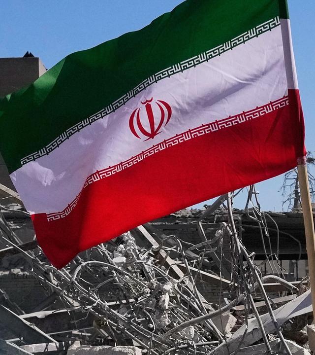 Eine Iran-Flagge vor einem eingestürzten Gebäude.