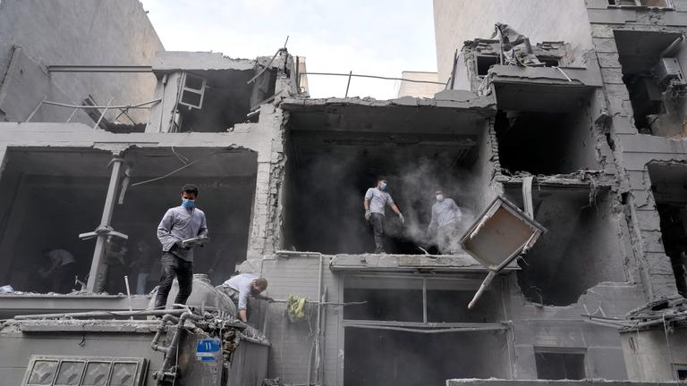 Menschen stehen in einer durch Krieg zerstörten Ruine im iranischen Teheran