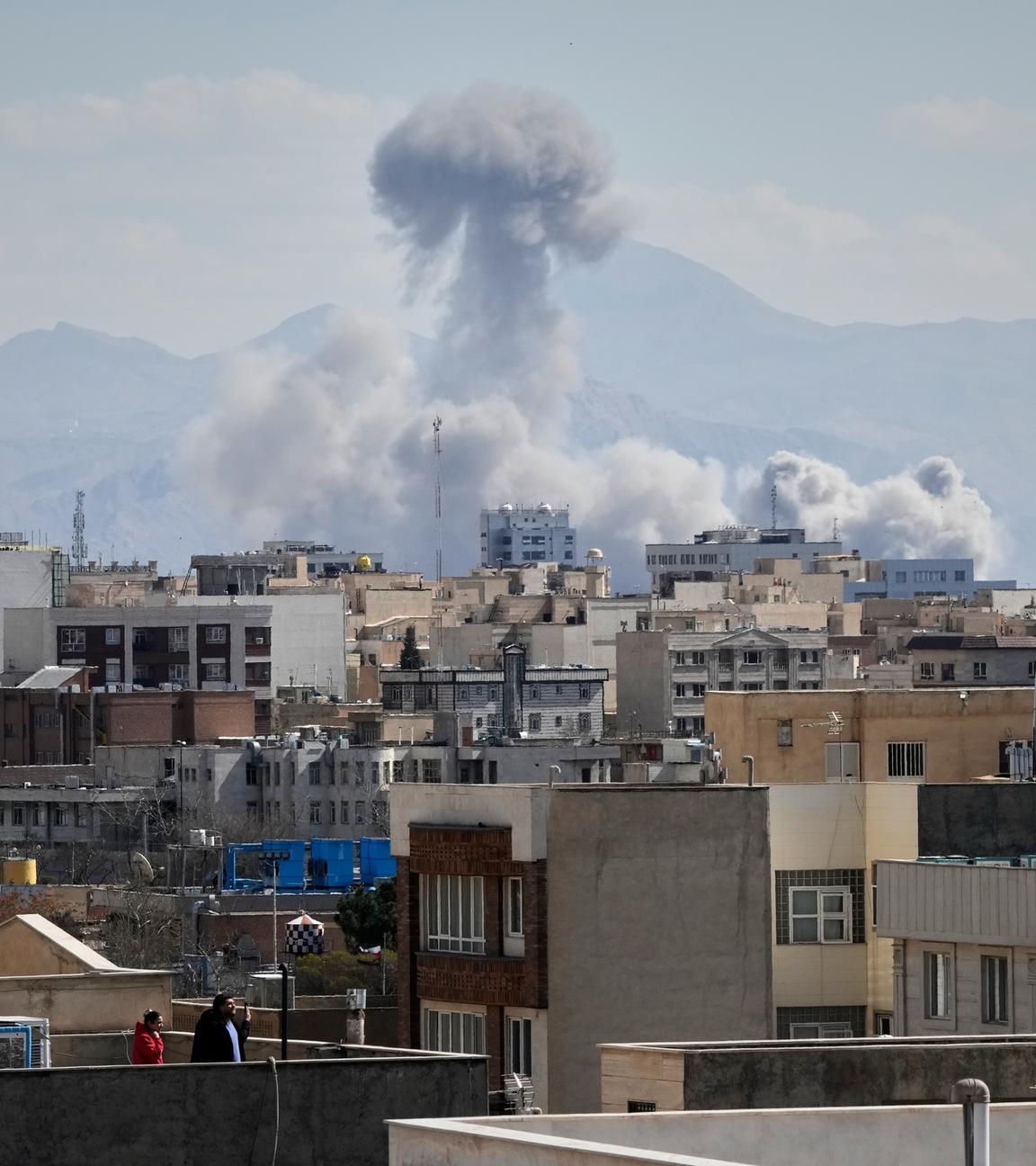 Menschen beobachten von einem Dach aus, wie nach einem Angriff in Teheran eine Rauchwolke aufsteigt.