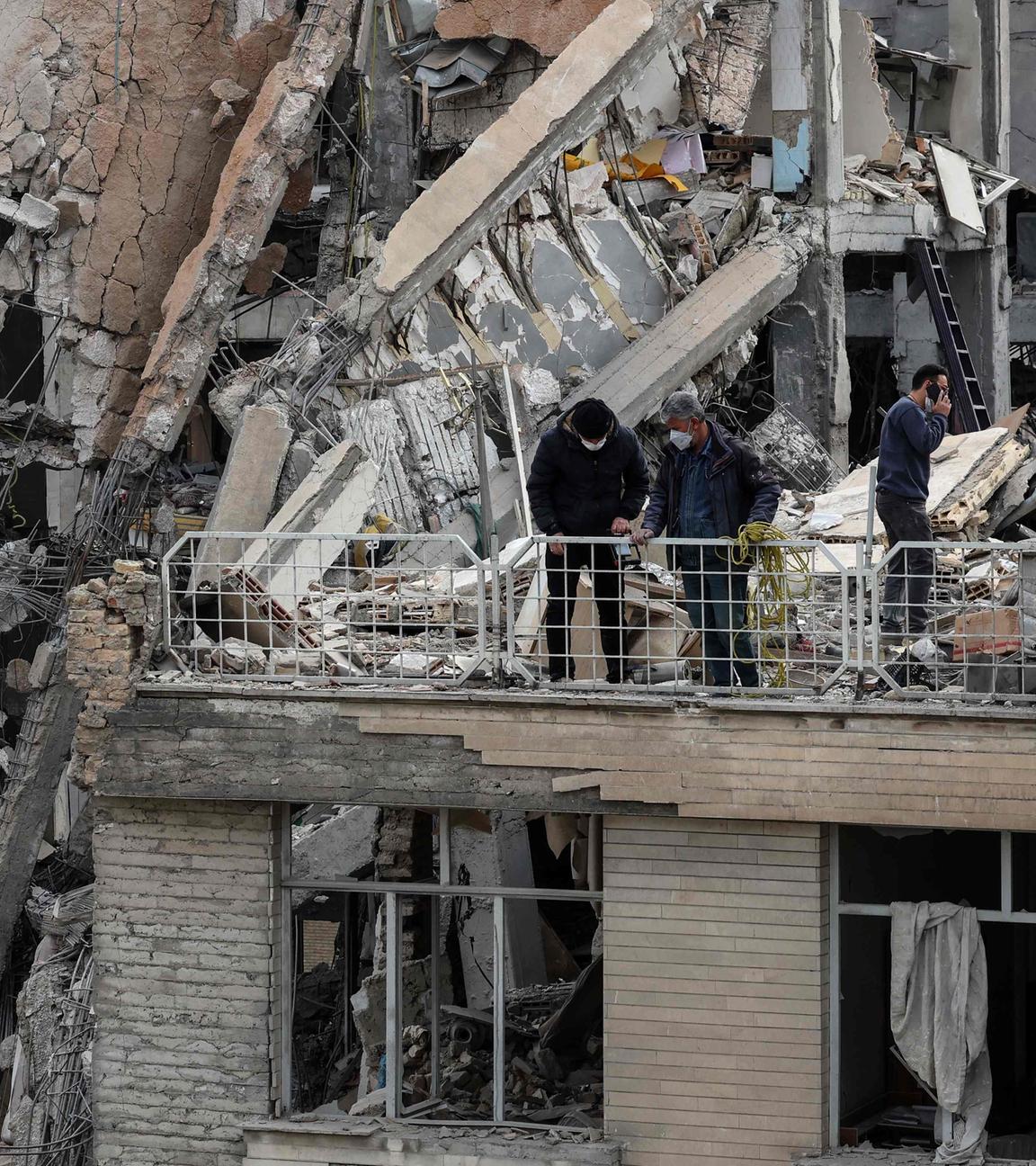 Iran, Teheran. Drei Menschen stehen auf dem Dach eines zerstörten Gebäudes.