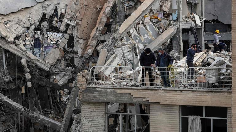 Iran, Teheran. Drei Menschen stehen auf dem Dach eines zerstörten Gebäudes.