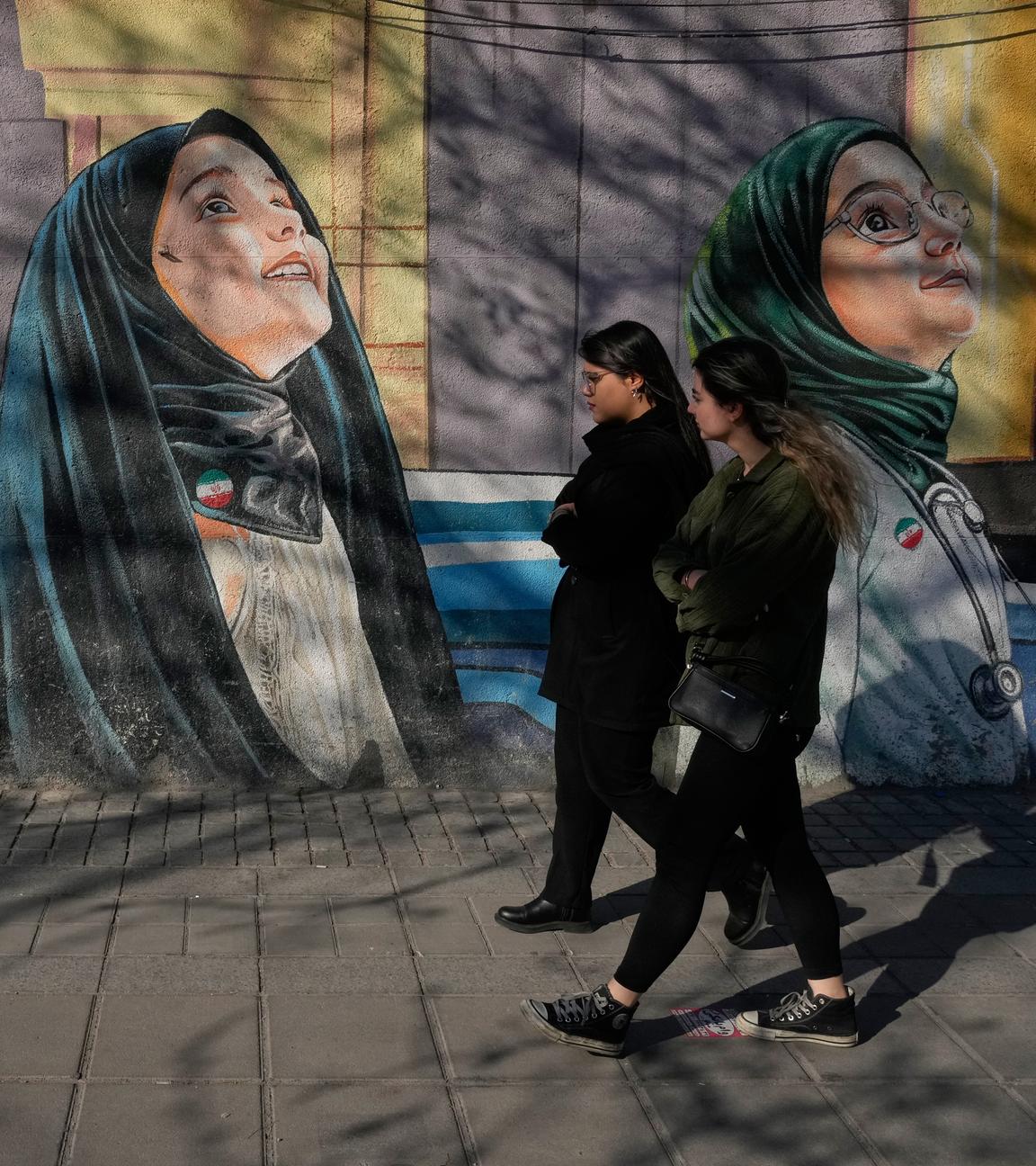 Frauen gehen an einem Gemälde an der Wand einer Mädchenschule im Zentrum von Teheran, Iran, vorbei. 