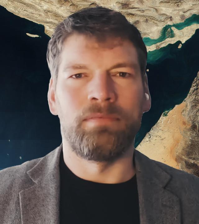 Dr. Moritz Brake im Vordergrund mittig im Bild und im Hintergrund ein Satellitenbild von der Straße von Hormus.