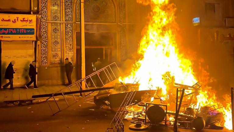 Flammen steigen am 10. Januar 2026 aus brennenden Trümmern mitten auf einer Straße in Gorgan auf.