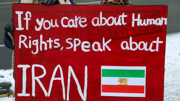Eine Frau hält ein Schild hoch, das auf die Umstände in Iran anspielt